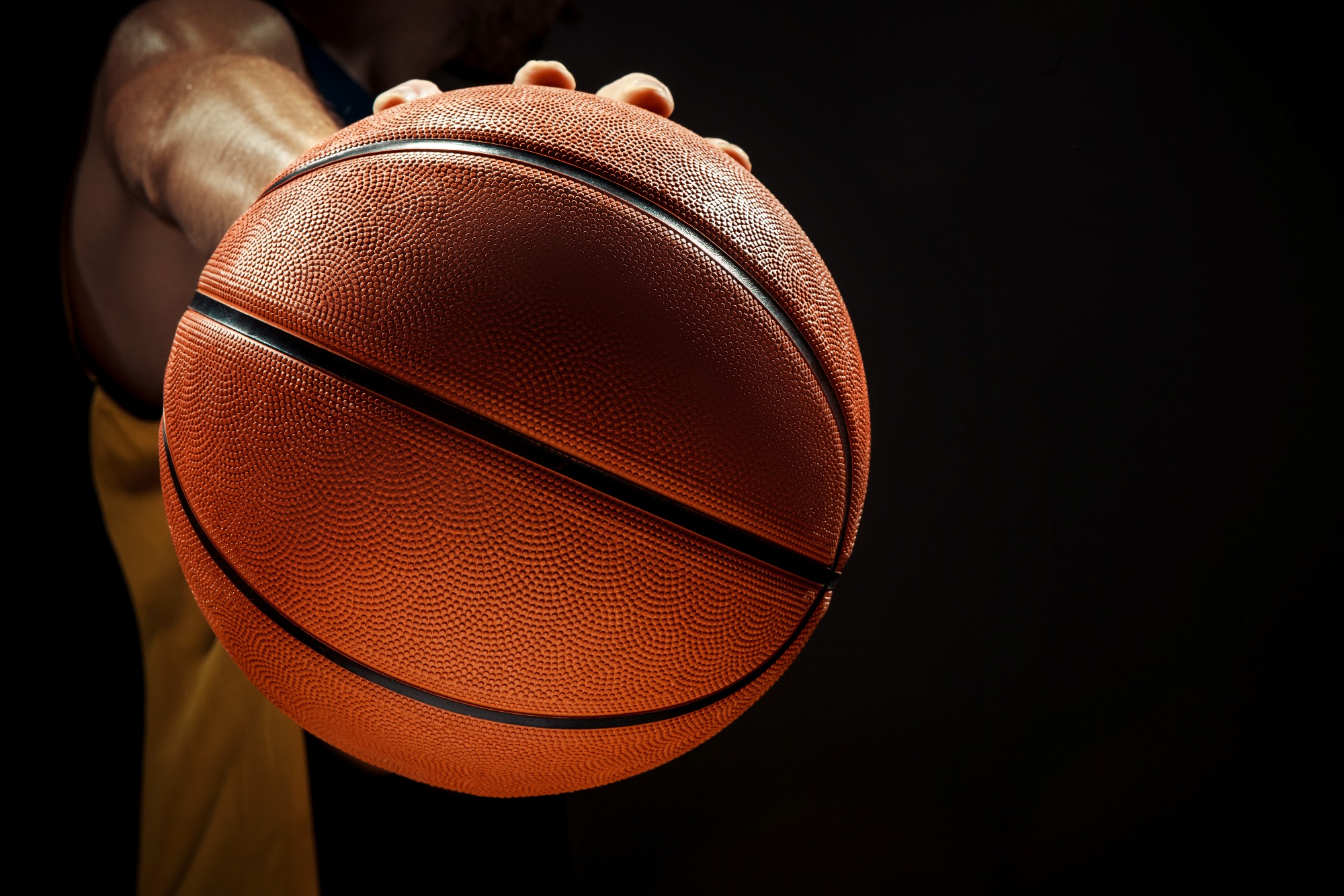 The silhouette view of a basketball player holding basket ball on black background. The hands and ball close up